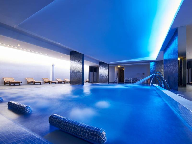 Moderní vnitřní bazén s modrým osvětlením a odpočinkovými zónami v hotelu.