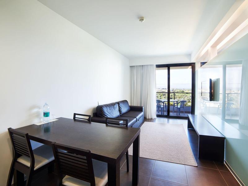 Světý obývací pokoj s jídelním stolem, koženou pohovkou a přístupem na balkon s výhledem.