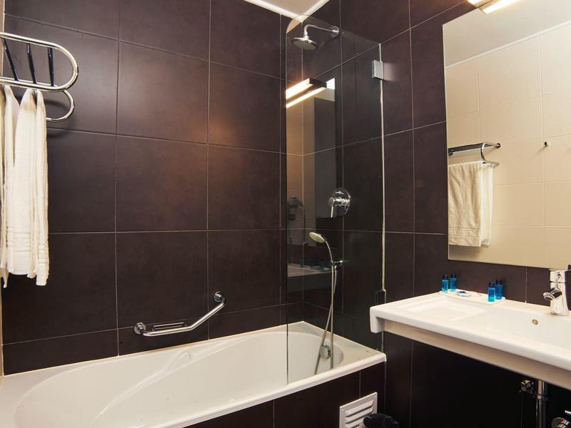 Moderní koupelna s vanou, sprchou a velkým zrcadlem na tmavých stěnách.