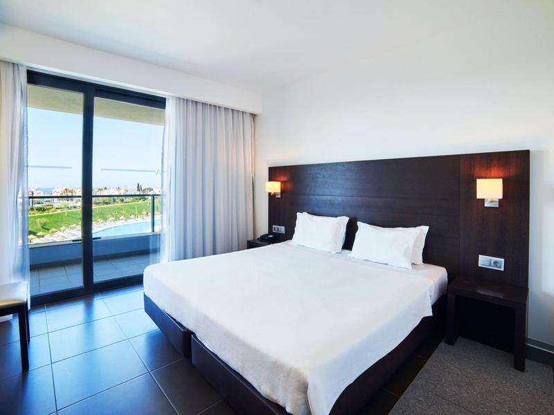 Moderní hotelový pokoj s velkou manželskou postelí a balkonem s výhledem na moře.