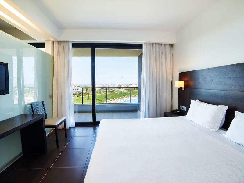 Moderní hotelový pokoj s velkou postelí a balkónovými dveřmi s výhledem na kanál.