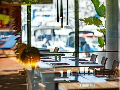 Leerer Außenbereich eines Cafés mit Tischen, Stühlen und Blick auf Hafen und Boote.