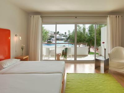 Helles Hotelzimmer mit zwei Einzelbetten, großem Fenster, grünem Teppich und weißem Sessel.