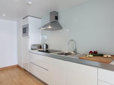 Moderne weiße Küchenzeile mit Edelstahlspüle, Dunstabzugshaube und Holzarbeitsfläche.