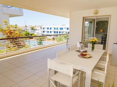 Große Terrasse mit weißem Tisch, vier Stühlen, Pflanzen und Blick auf benachbarte Gebäude bei Sonnenlicht.