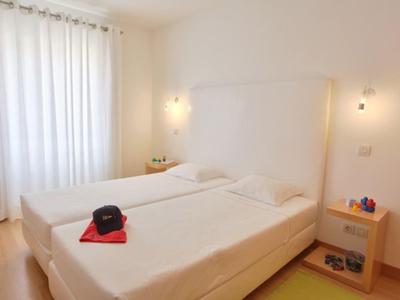 Helles Schlafzimmer mit zwei Einzelbetten, weißen Vorhängen und seitlichen Nachttischen.