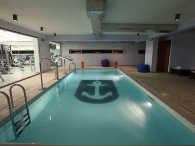 Innen-Schwimmbad mit Anker-Motiv am Beckenboden, Holzverkleidung und Sitzkissen an der Wand.