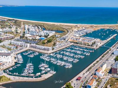 Küstenstadt mit Hafen, vielen Booten und langen Sandstränden unter blauem Himmel.