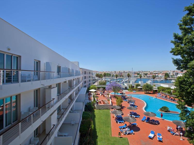 Moderner Hotelbau mit Balkonen und einladendem Poolbereich unter klarem blauem Himmel.