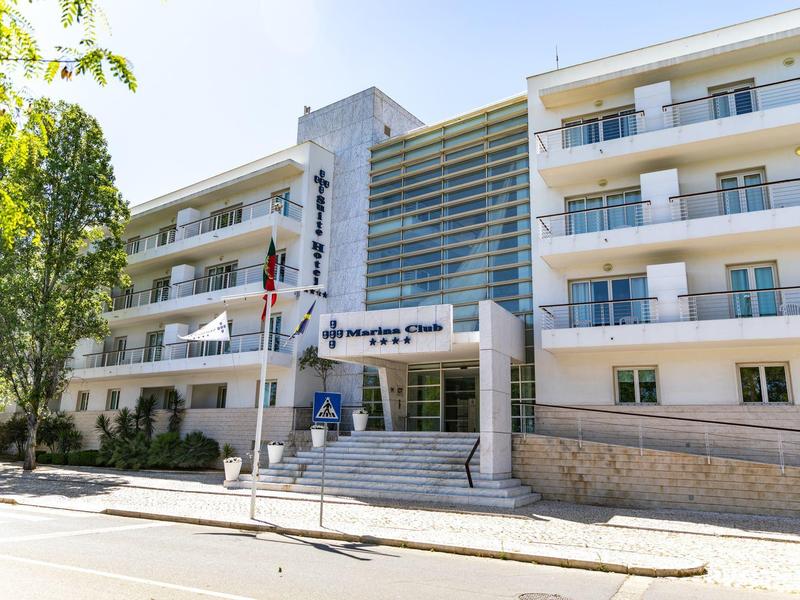 Modernes Bürogebäude mit Glasfront, mehreren Stockwerken und Fahnen am Eingang bei Sonnenschein.