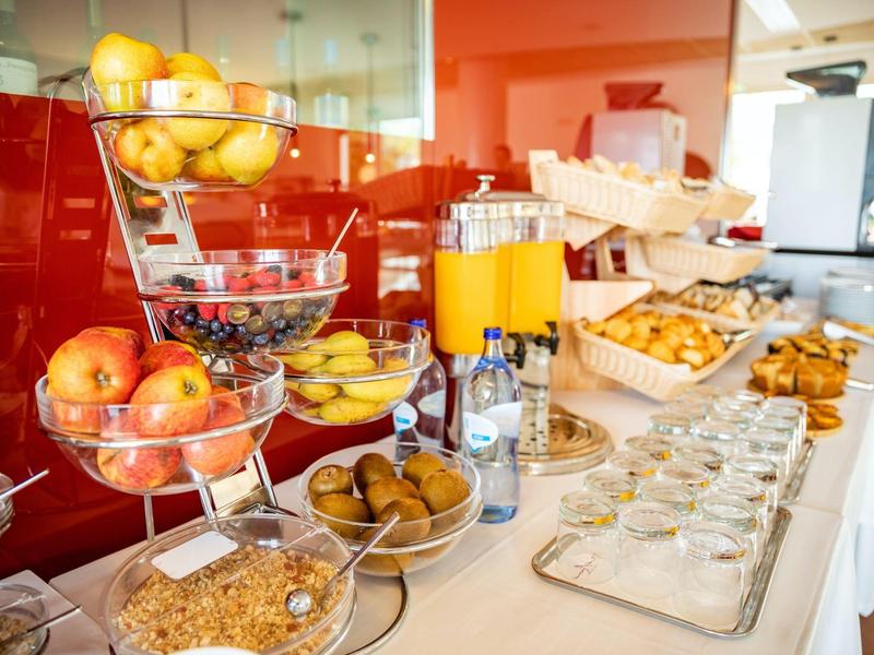 Buffet mit frischem Obst, Müsli, frischem Gebäck und Orangen Saft auf weiß gedecktem Tisch.