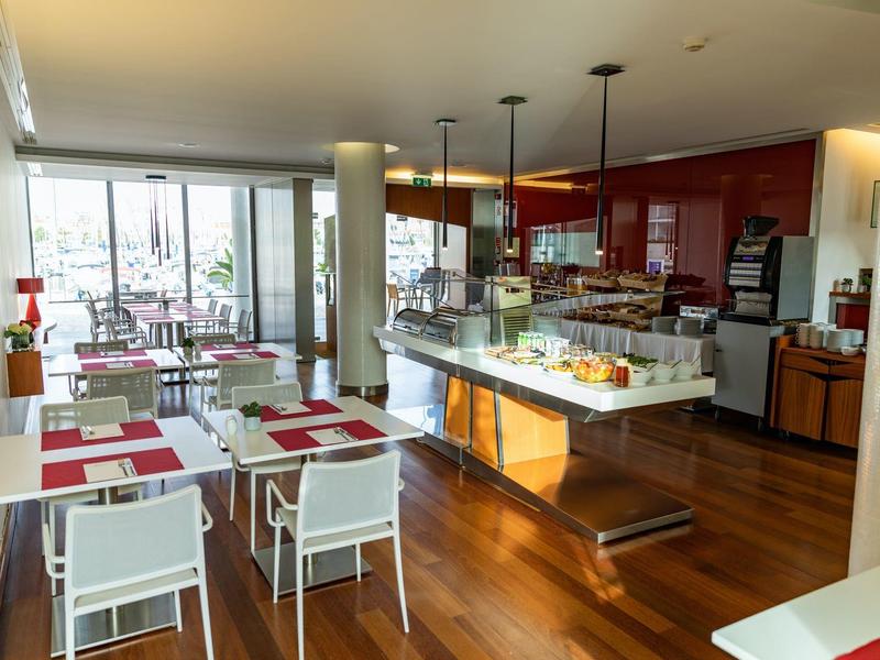 Helles, modernes Café mit Holzboden, weißen Tischen, roten Wandakzenten und Buffetbereich.