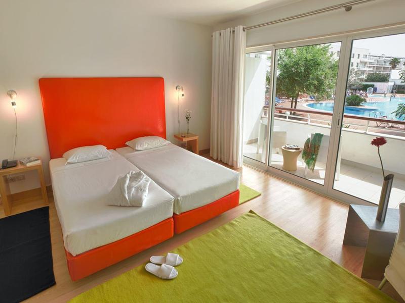 Modernes Schlafzimmer mit zwei Einzelbetten, orangem Kopfteil und Zugang zu Balkon mit Poolblick.