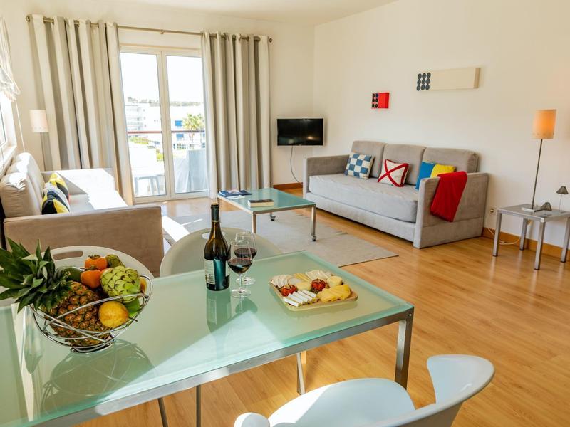 Helles Wohnzimmer mit Glas-Tisch, Obstkorb, zwei Sofas, Holzlaminatboden und Balkon in sanften Farben.