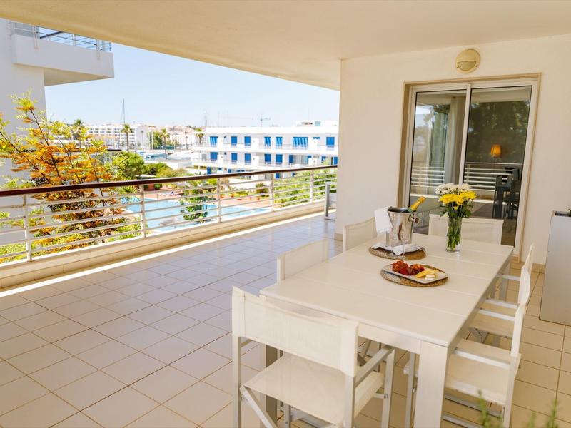 Große Terrasse mit weißem Tisch, vier Stühlen, Pflanzen und Blick auf benachbarte Gebäude bei Sonnenlicht.