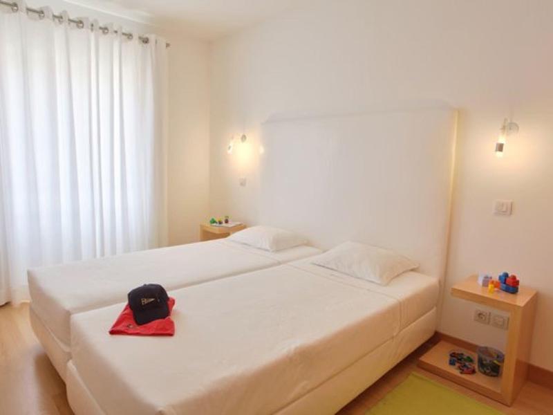 Helles Schlafzimmer mit zwei Einzelbetten, weißen Vorhängen und seitlichen Nachttischen.