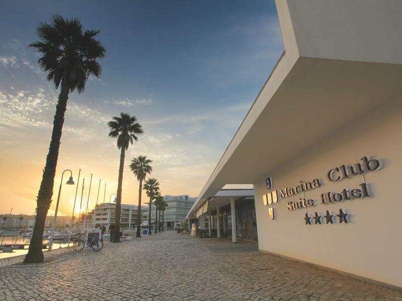 Moderne Hotelanlage am Wasser mit Palmen, Strandpromenade und Abendhimmel.