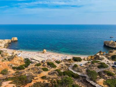 Côte rocheuse avec petite plage de sable et mer bleue claire sous un ciel ensoleillé.