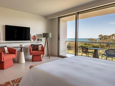 Chambre d'hôtel moderne avec vue sur la mer, balcon et décoration élégante aux tons rouges et blancs.