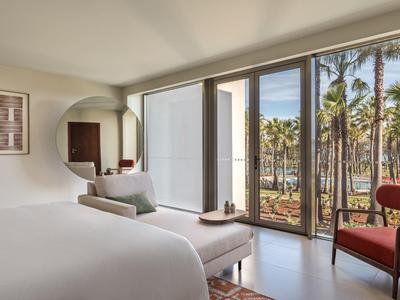 Chambre d'hôtel moderne avec grand lit et vue sur les palmiers à travers de grandes fenêtres.