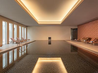 Piscine intérieure moderne avec chaises longues et éclairage indirect au plafond aux tons chauds.