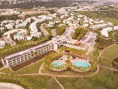 Vue aérienne d'un grand complexe de vacances avec piscines, bâtiments environnants et espaces verts.