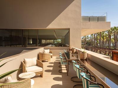 Terrasse d'hôtel spacieuse avec sièges confortables et vue sur des palmiers.