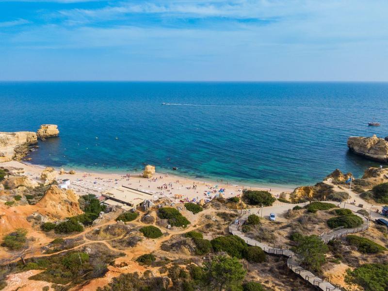 Côte rocheuse avec petite plage de sable et mer bleue claire sous un ciel ensoleillé.