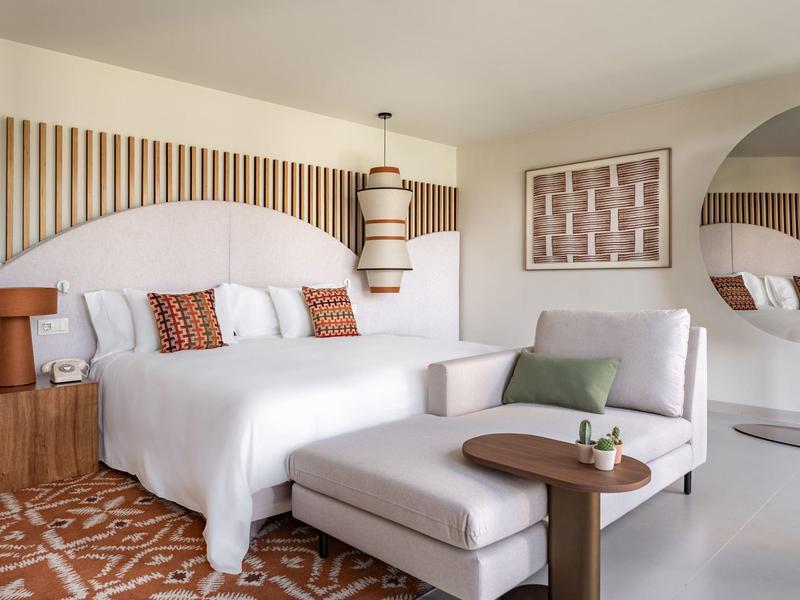 Chambre d'hôtel moderne avec grand lit, coin salon et décoration élégante aux couleurs chaudes.