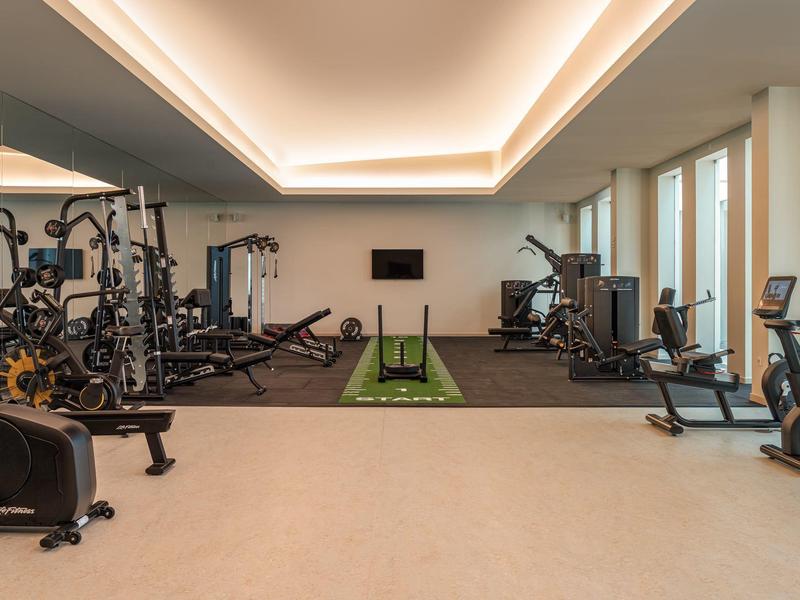 Salle de sport moderne avec haltères, équipements cardio et une bande d'entraînement verte au centre.