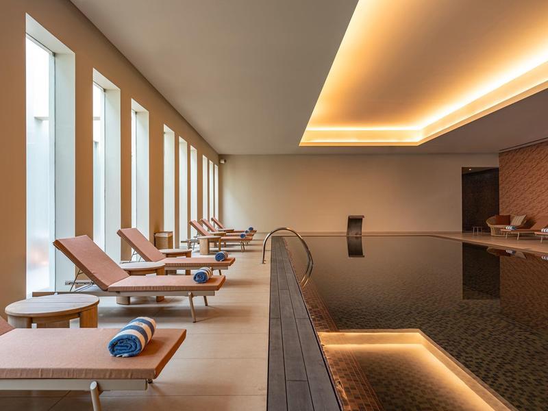 Espace piscine intérieure élégant avec chaises longues confortables et éclairage chaud au plafond.