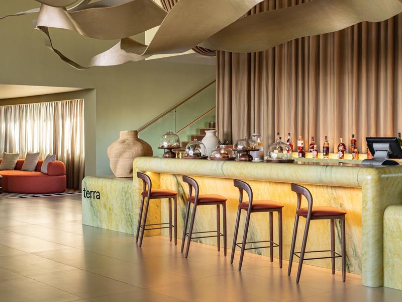 Espace bar d'hôtel moderne avec des tabourets en bois confortables et un éclairage créatif au plafond.