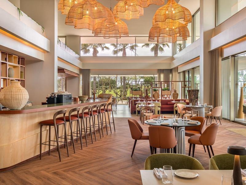 Restaurant moderne avec sol en bois, bar avec tabourets et grandes fenêtres donnant sur le jardin.