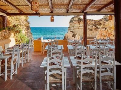 Area pranzo aperta con sedie bianche e vista sul mare e sulle rocce sullo sfondo.