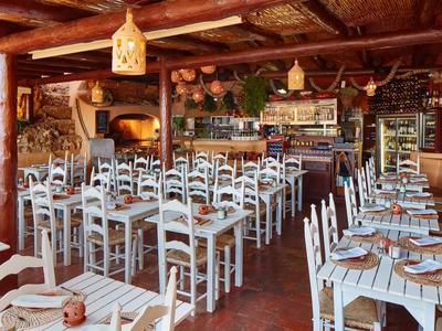 Ristorante rustico con tavoli e sedie in legno bianco, soffitto in legno e forno a legna.
