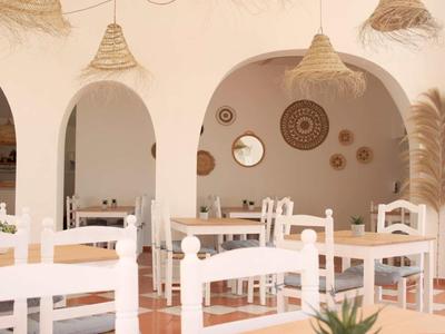 Ristorante luminoso con sedie in legno bianche, tavoli e cesti decorativi alle pareti.