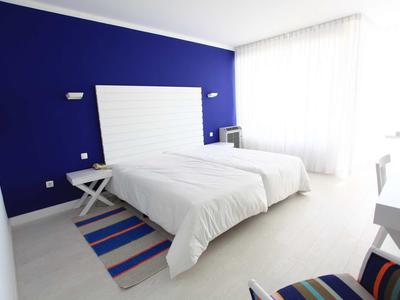 Camera d'hotel moderna con due letti singoli, parete blu e grande finestra.