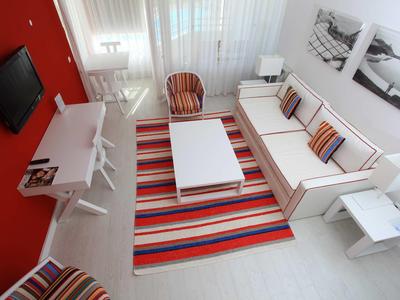 Soggiorno luminoso con divano bianco, tappeto colorato e parete rossa in camera d'albergo.