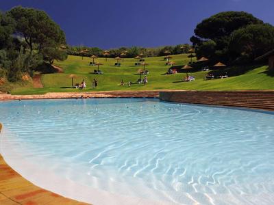 Piscina con acqua limpida di fronte a un paesaggio verde e collinare sotto un cielo azzurro.