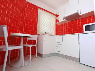 Piccola cucina con armadi bianchi e pareti con piastrelle rosse, con tavolo e due sedie.