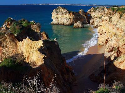 Piccola baia sabbiosa tra alte scogliere sulla costa con acqua azzurra limpida.