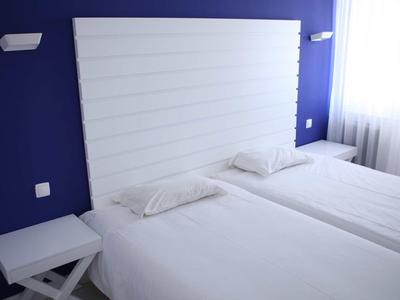 Due letti singoli con lenzuola e cuscini bianchi davanti a una parete blu e una testiera bianca.