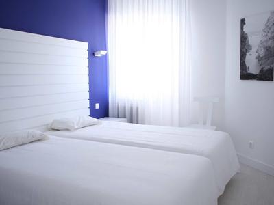 Camera d'hotel luminosa con due letti singoli e parete accentuata blu.