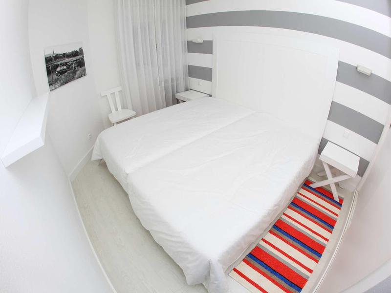 Piccola camera da letto con due letti singoli uniti, mobili bianchi e parete a righe.