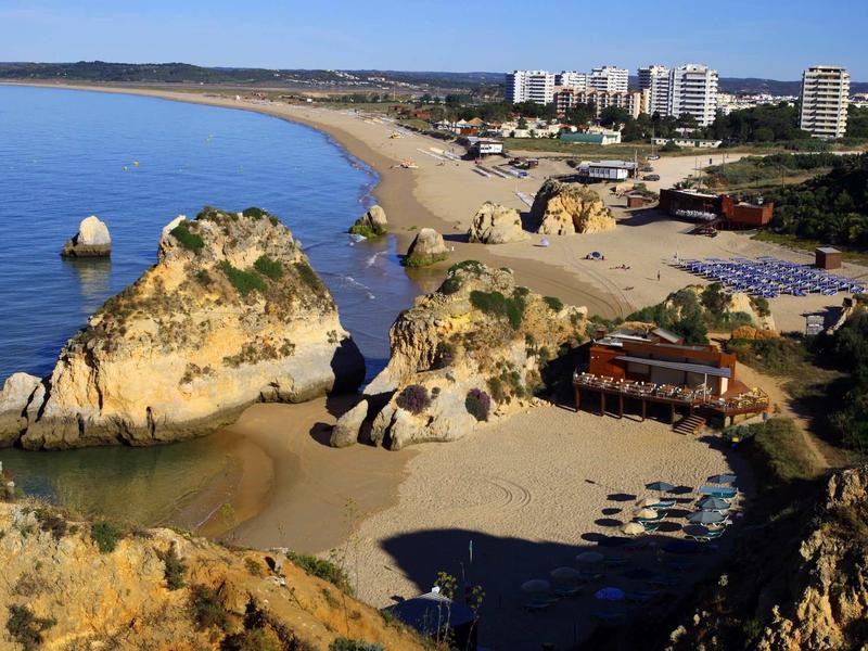 Piccola spiaggia di sabbia con rocce e hotel sullo sfondo lungo la costa.