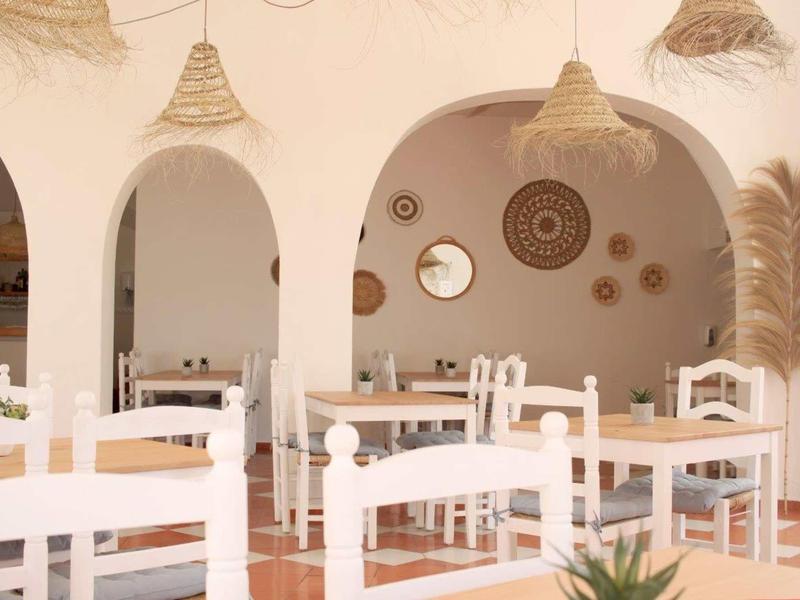 Ristorante luminoso con sedie in legno bianche, tavoli e cesti decorativi alle pareti.