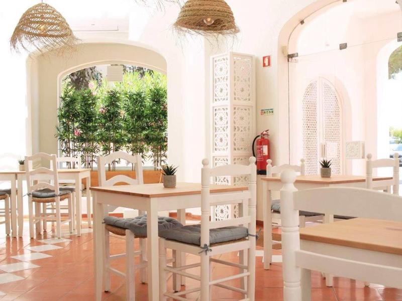 Ristorante luminoso e arioso con mobili bianchi in legno e lampade a cesta sospese.