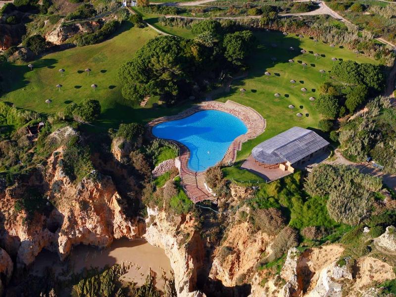 Vista aerea di un hotel con piscina blu in un paesaggio costiero roccioso.