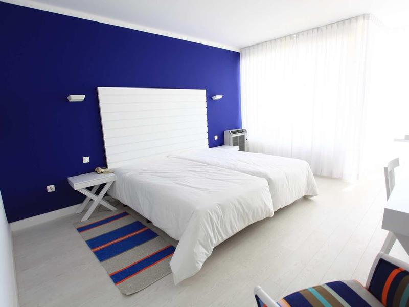 Camera d'hotel moderna con due letti singoli, parete blu e grande finestra.