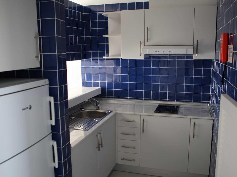 Cucina compatta con armadi bianchi, pareti piastrellate blu e un lavandino vicino alla finestra.